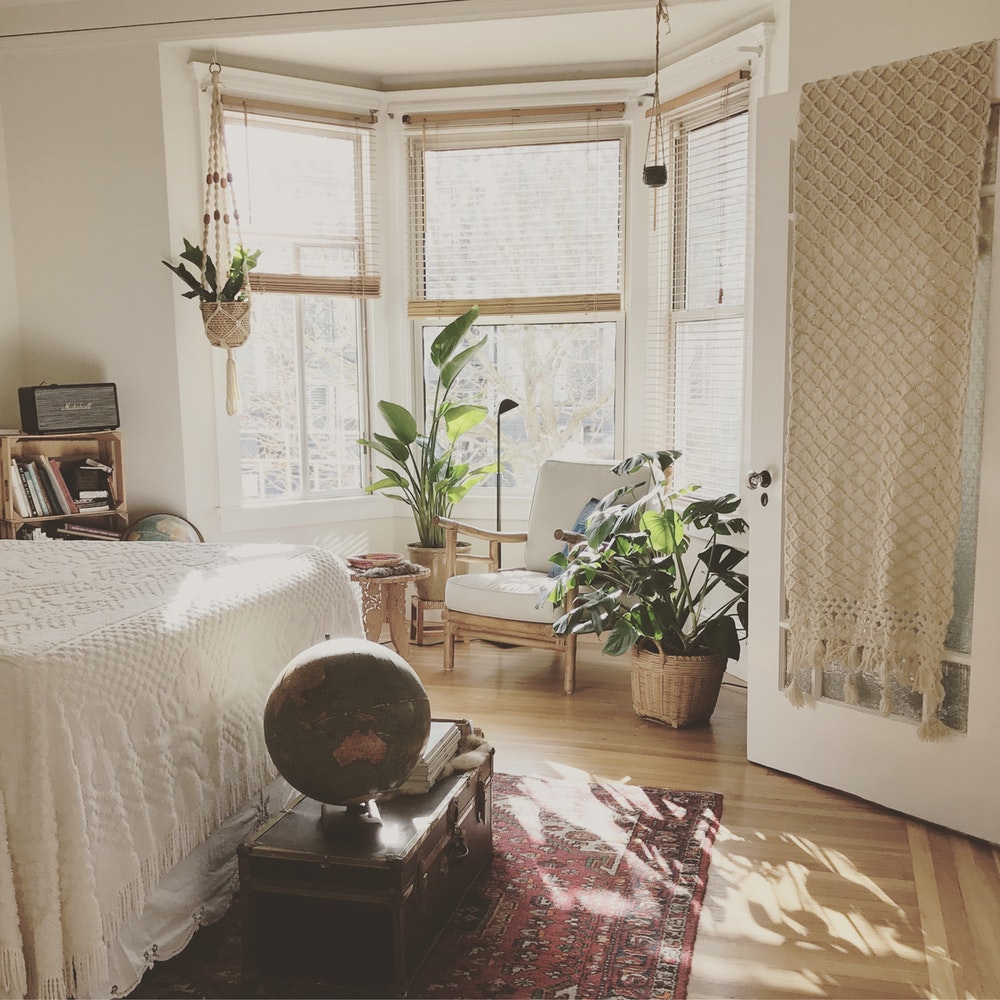 a bohemian styled bedroom with hanging planters and two medium sized potted plants nestled infront of a bay window